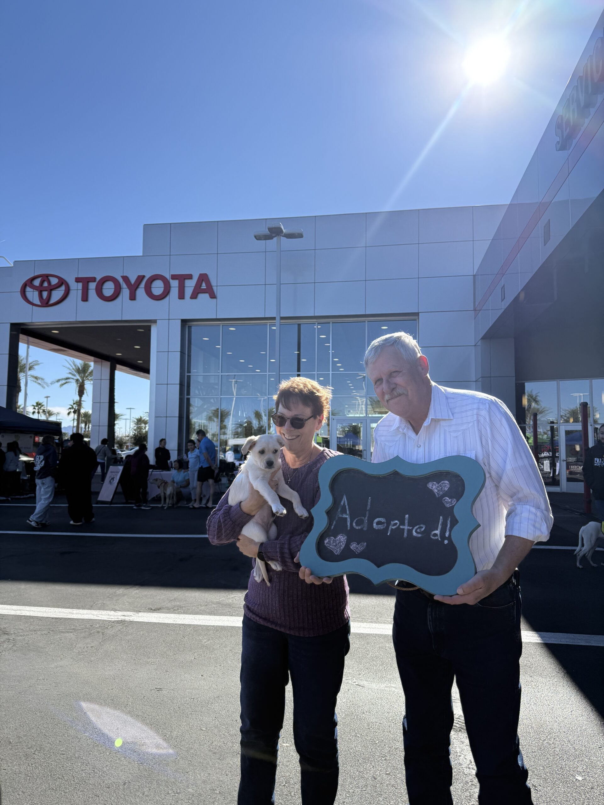 Two people holding an 'Adopted' sign holding their dog.